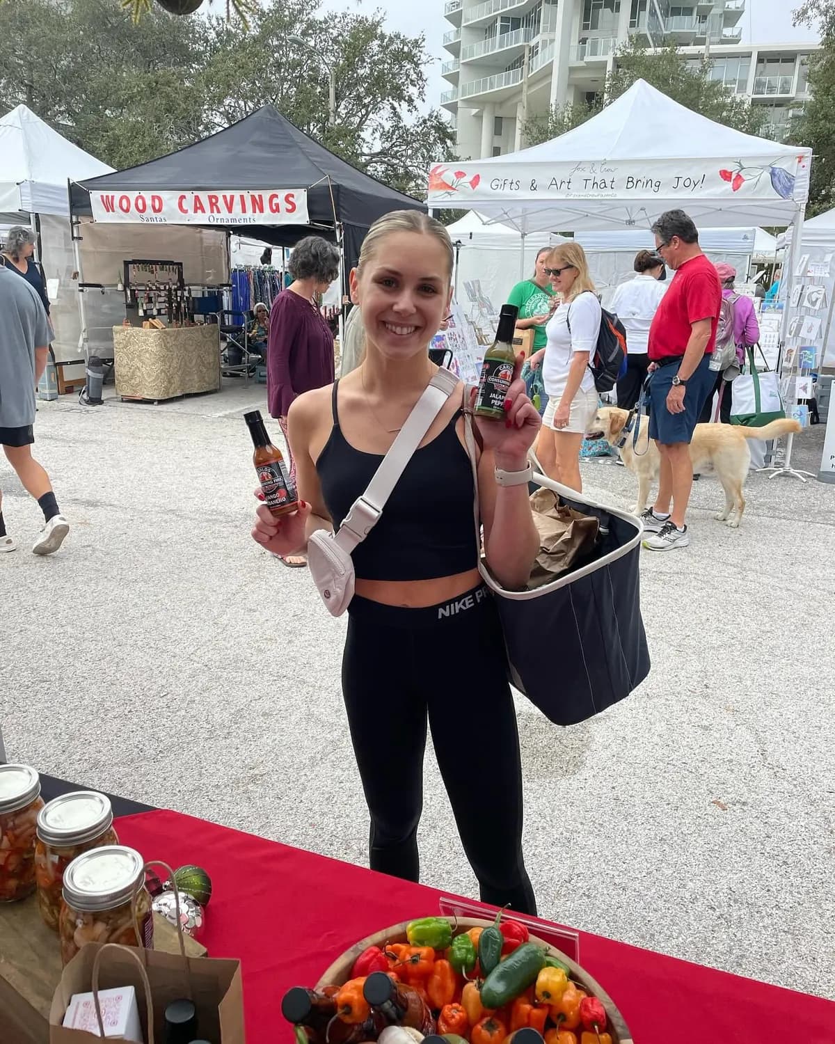 Fan holding up two sauce bottles at a busy outdoor farmers market